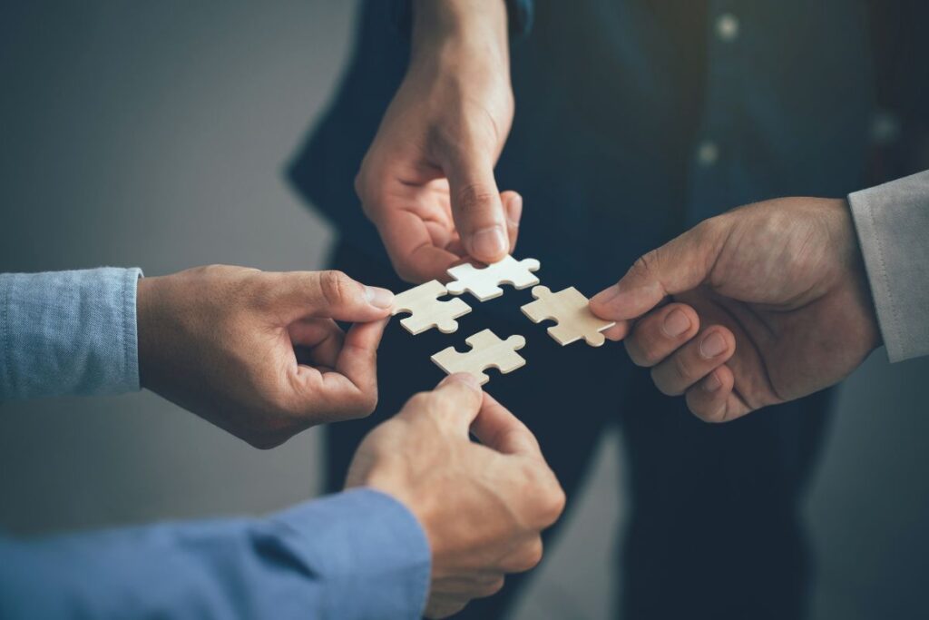 Mehrere Hände setzen gemeinsam ein Puzzle zusammen als Symbol für die Zusammenarbeit der ACREDIA Group.